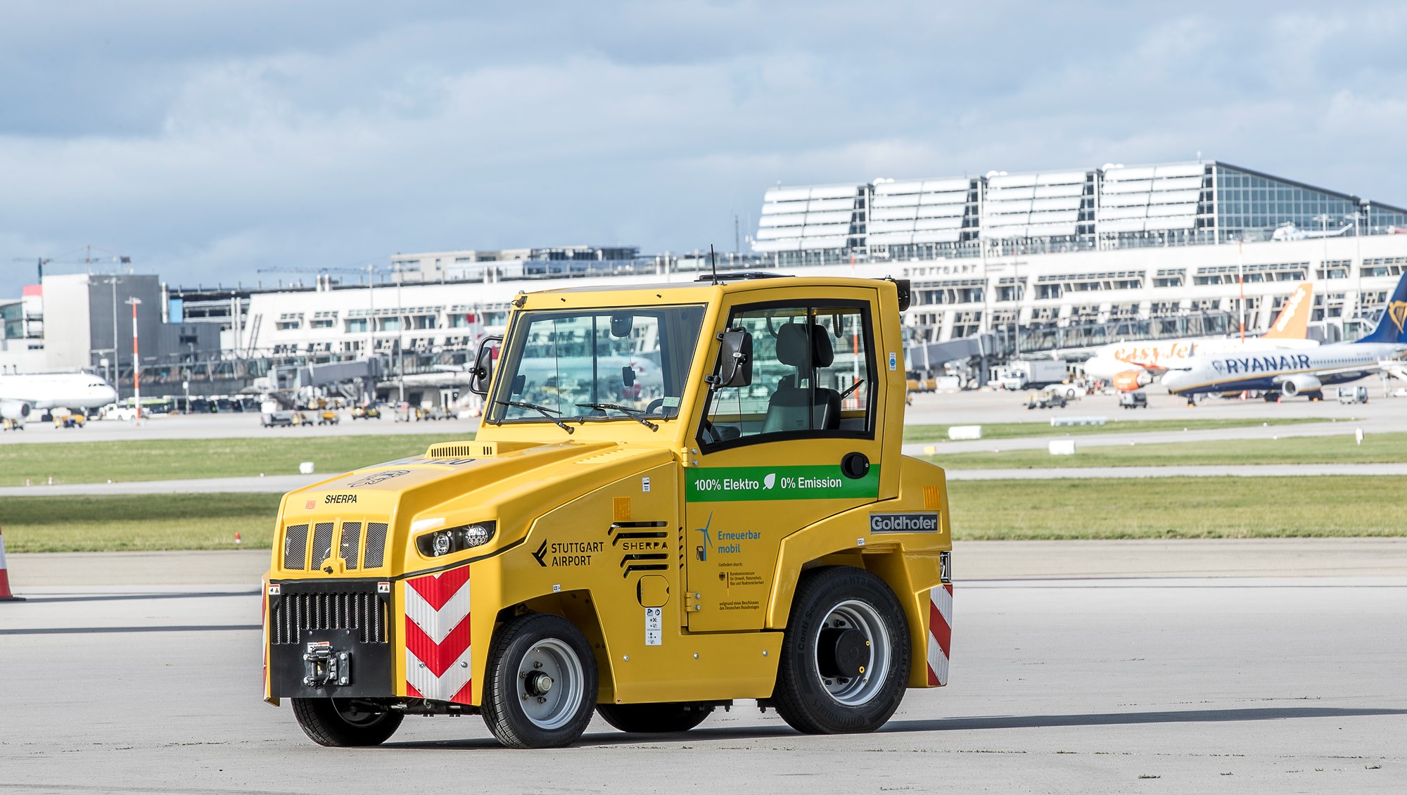 Ein elektrisch betriebener Cargo-Schlepper steht auf dem südlichen Stuttgarter Flughafenvorfeld. Im Hintergrund stehen die Terminalgebäude. 