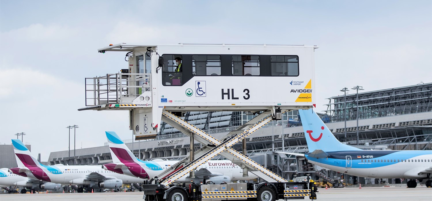 Ein elektrisch betriebener Medical-Highloader steht ausgefahren auf dem Stuttgarter Flughafenvorfeld. Im Hintergrund parken Flugzeuge. 